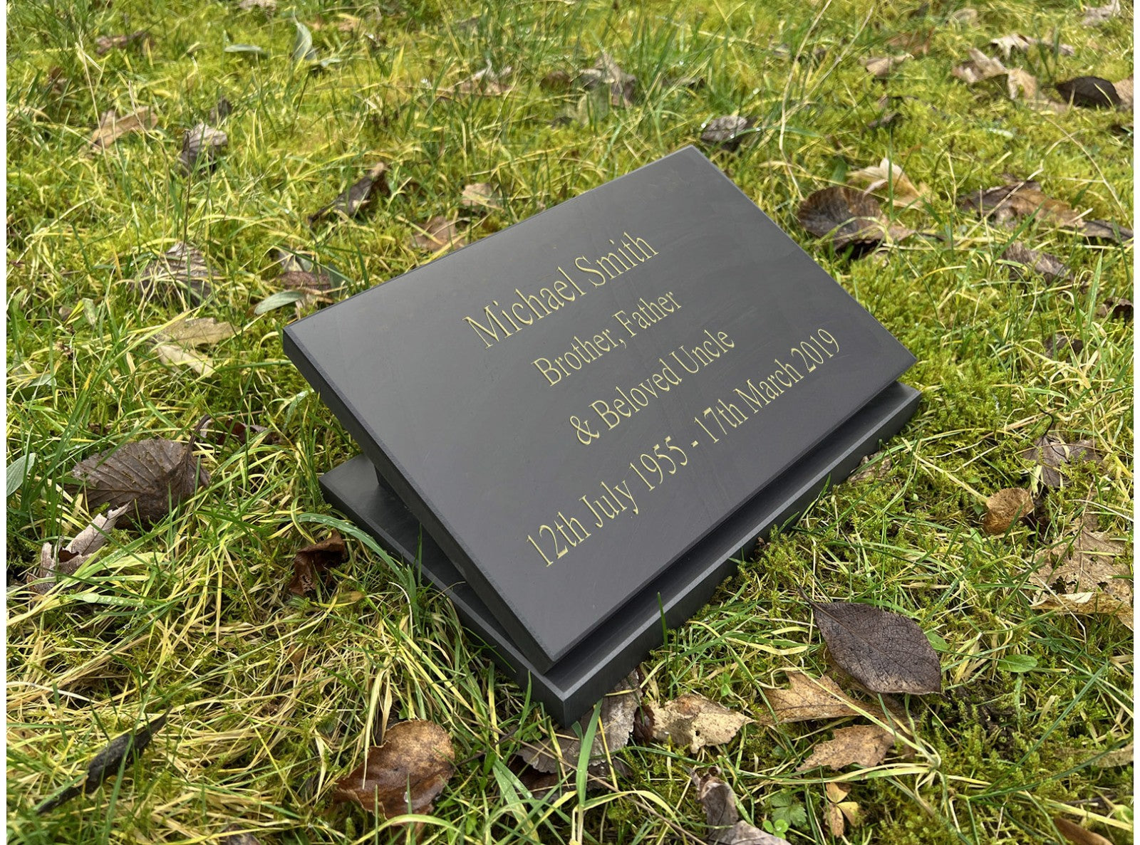 A 200mm x 300mm Welsh slate memorial plaque that lays on the ground, sentimental words deep engraved and colour filled on it