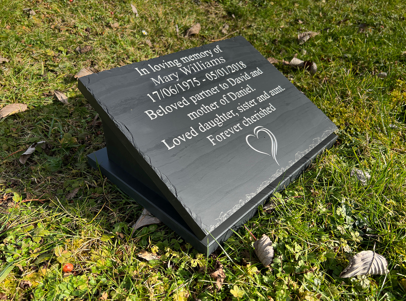 A 300mm x 400mm Welsh slate memorial plaque that lays on the ground, sentimental words deep engraved and colour filled on it