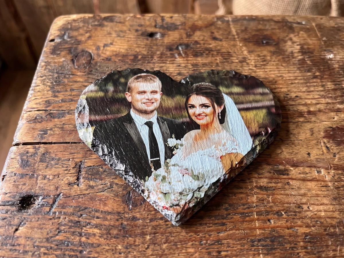 A heart-shaped rustic stone plaque featuring a custom printed photo of a bride and groom, displayed on a weathered wooden surface.