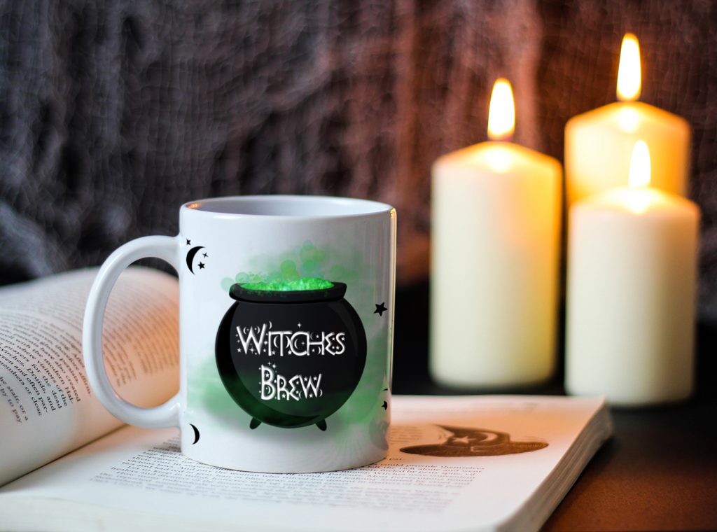White ceramic mug with the illustration of a green and black cauldron saying witches brew