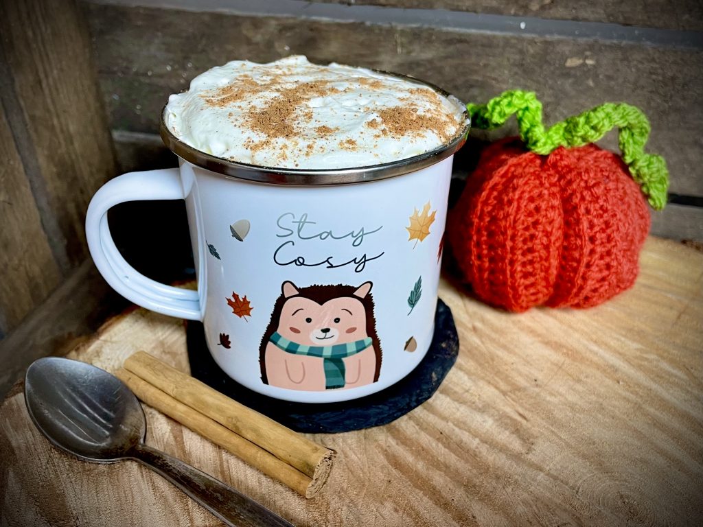 White enamel mug filled with pumpkin spice latte topped with cream and grated cinnamon