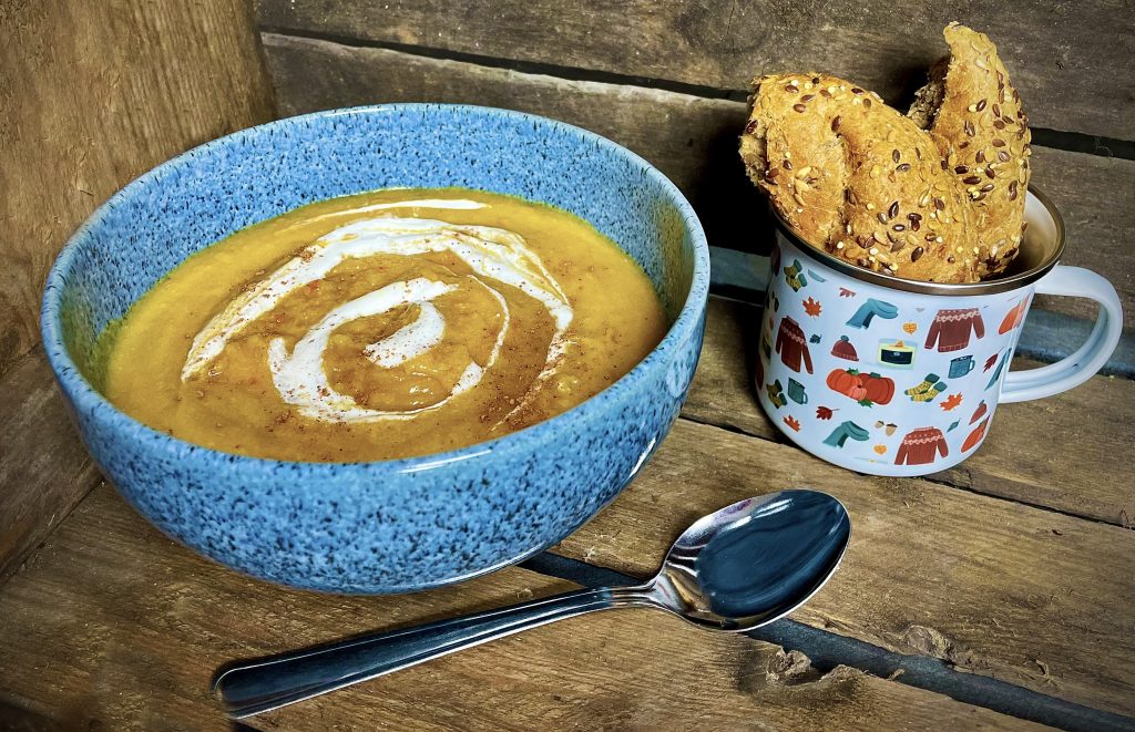 Bowl of pumpkin soup served in a blue bowl with crusty bread and a spoon