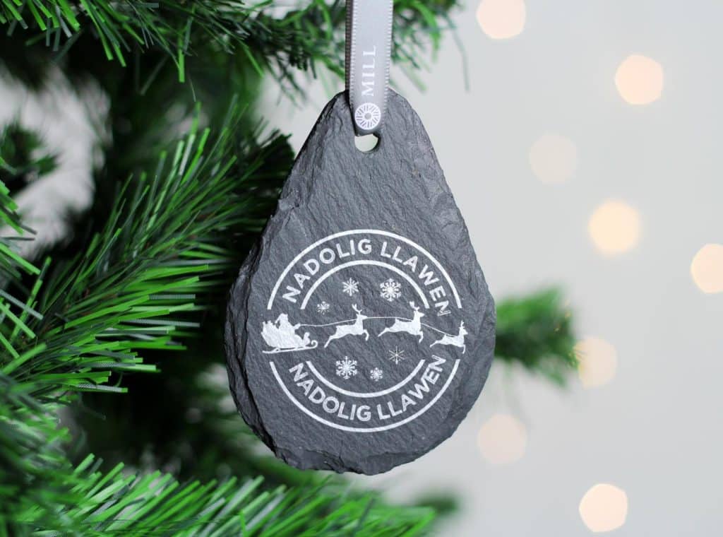 welsh slate teardrop shape christmas decoration hung on a tree with the words nadolig llawen and santa and his reindeers
