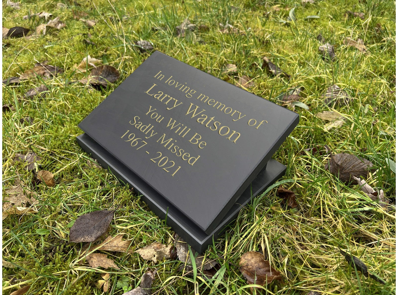 A 200mm x 150mm Welsh slate memorial plaque that lays on the ground, sentimental words deep engraved and colour filled on it